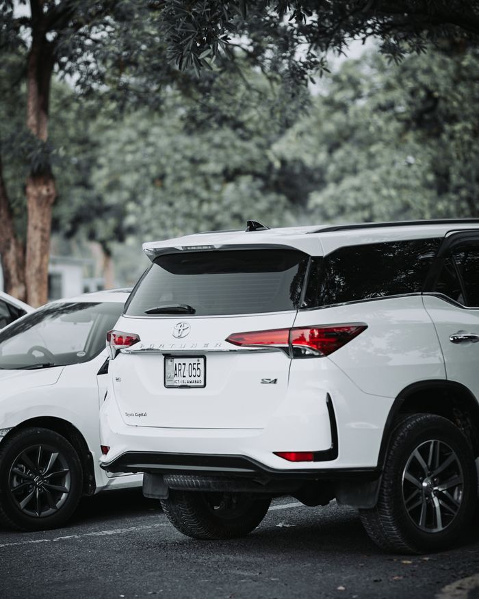 why-choose-us A white Toyota Fortuner parked outdoors in a lush green setting, highlighting luxury and style.