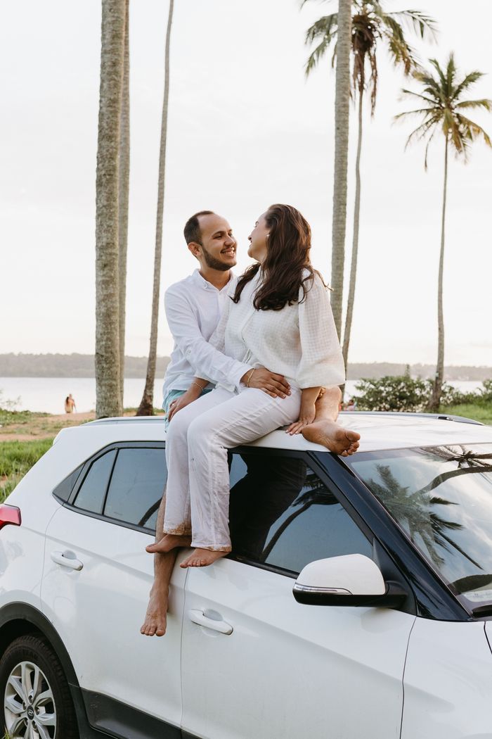 services-02 Couple in white outfits sitting on a car roof near palm trees by the beach, enjoying a sunny day.