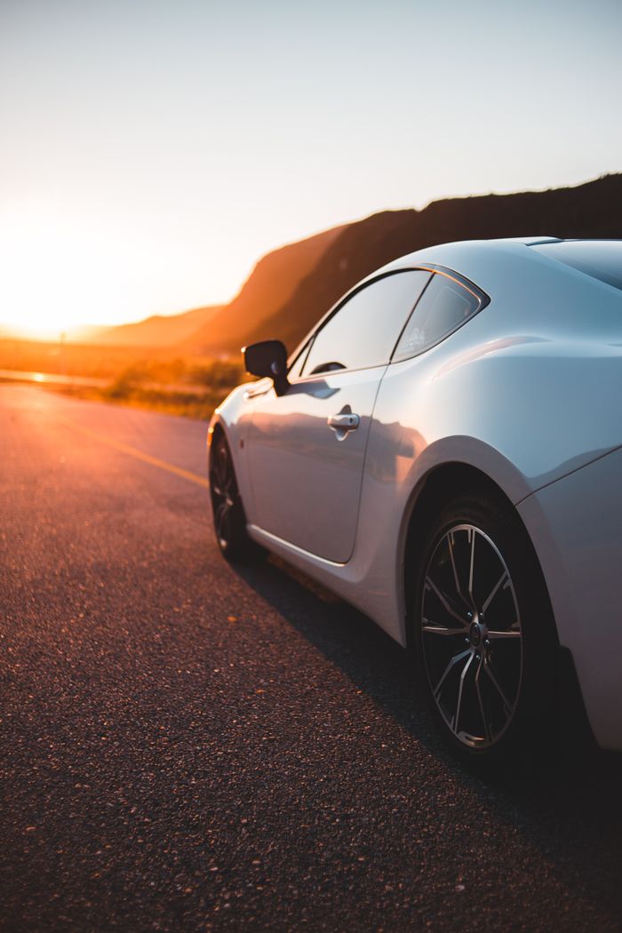 who-we-are Shiny white coupe automobile on paved route in bright light of sunset in mountains