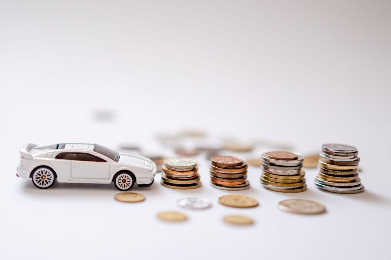 team-02 White toy sports car beside stacks of coins on a white background, emphasizing savings and finance.